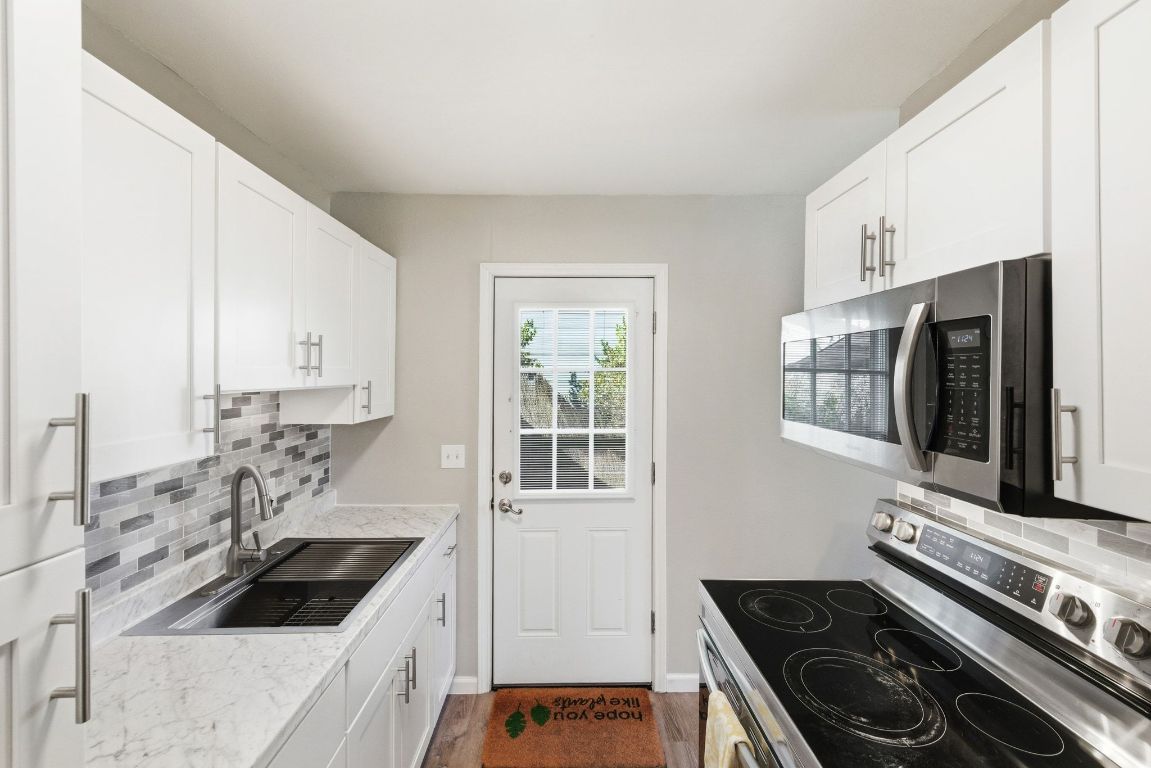 4615 Munson Street Austin, TX 78721 - Photo 15 of 27 Kitchen with backsplash, stainless steel appliances, white cabinets, light stone countertops, and dark wood-type flooring