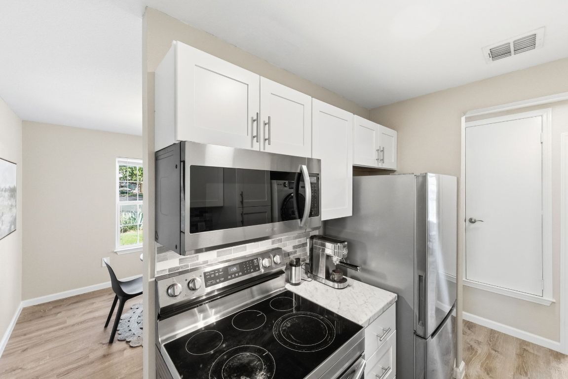 4615 Munson Street Austin, TX 78721 - Photo 17 of 27 Kitchen with appliances with stainless steel finishes, white cabinetry, light wood-type flooring, and backsplash