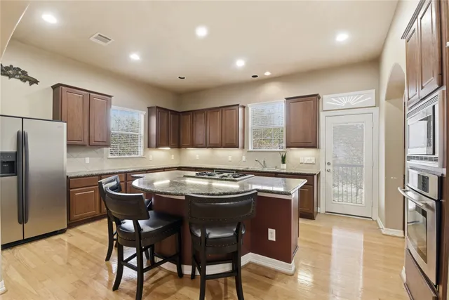 a kitchen with stainless steel appliances granite countertop a stove a refrigerator a sink a dining table and chairs