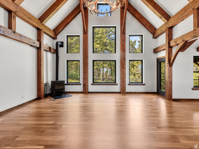 1225 Old Oregon Road Soda Springs, ID 83276 - Photo 6 of 67 Great room featuring vaulted ceilings with exposed wood beams, a central antler chandelier, wood-finish flooring, a freestanding wood-burning stove, and multiple large windows
