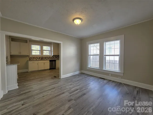 an empty room with wooden floor and a kitchen