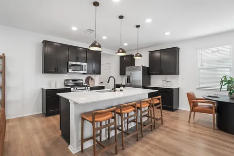 a kitchen with stainless steel appliances a stove a sink a microwave a refrigerator a dining table and chairs