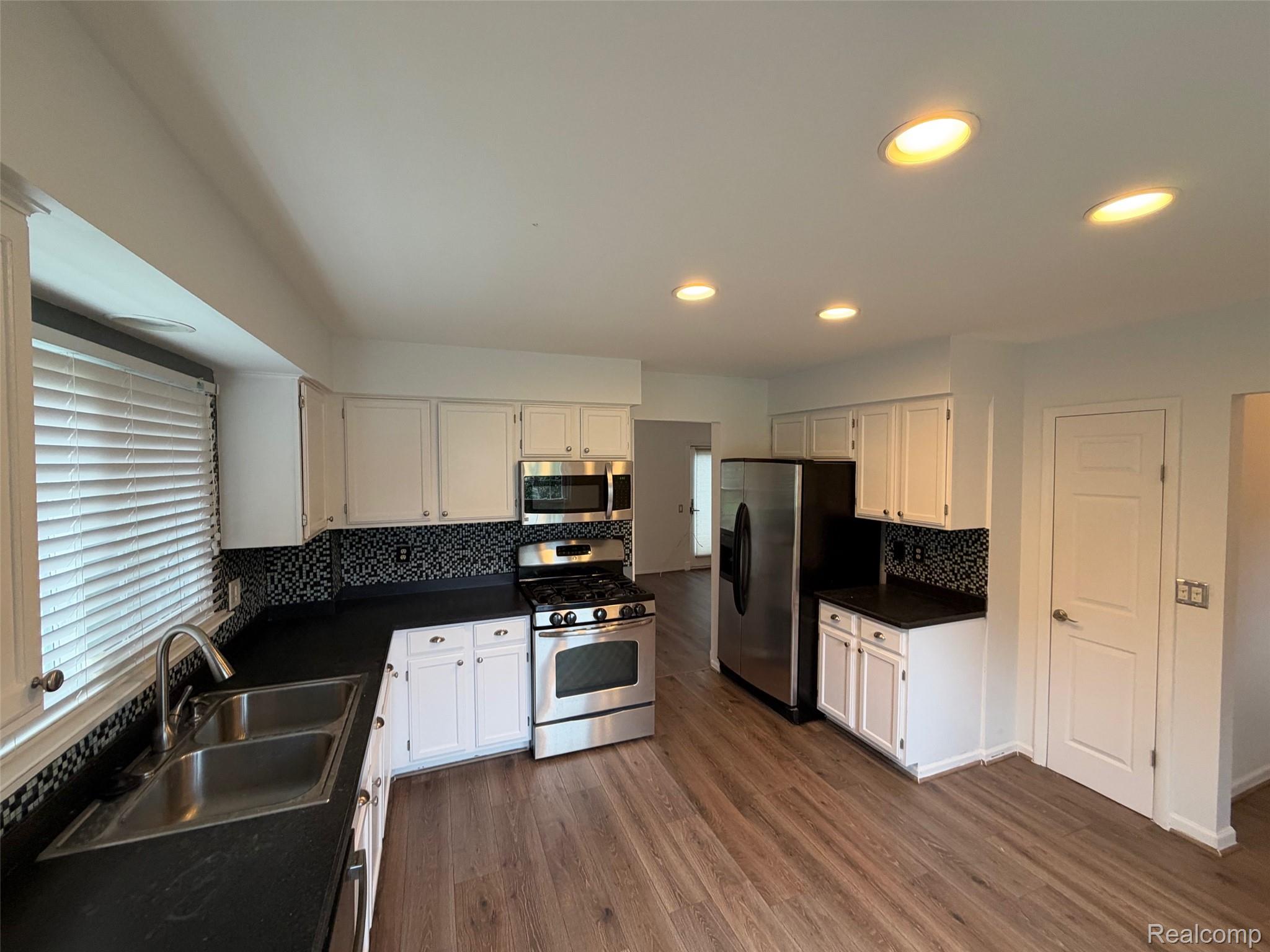24525 Jamestowne Road Novi, MI 48375 - Photo 6 of 20 Kitchen featuring wood-finish flooring, white cabinetry, black countertops, stainless steel appliances, and recessed lighting