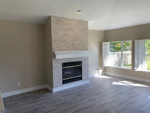 an empty room with wooden floor fireplace and windows