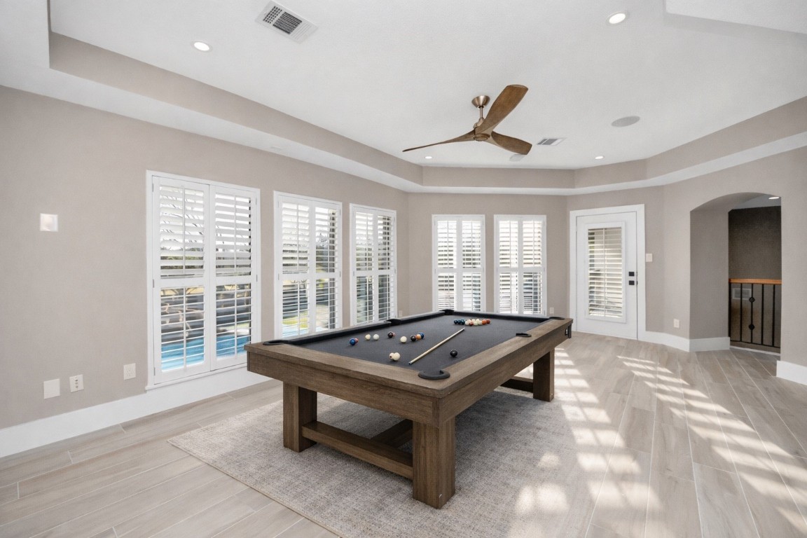2211 Braer Ridge Drive Katy, TX 77494 - Photo 15 of 50 Bright and spacious game room featuring a sleek pool table, large windows with plantation shutters, and elegant light wood flooring. The ceiling fan adds a modern touch, and there's easy access to the outdoors through the glass door. Perfect for entertainment and relaxation.