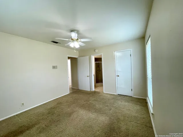 an empty room with chandelier fan and windows