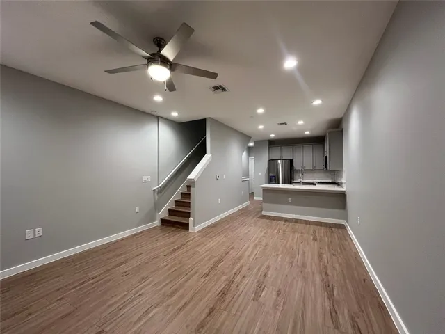 a view of an empty room with wooden floor and a ceiling fan