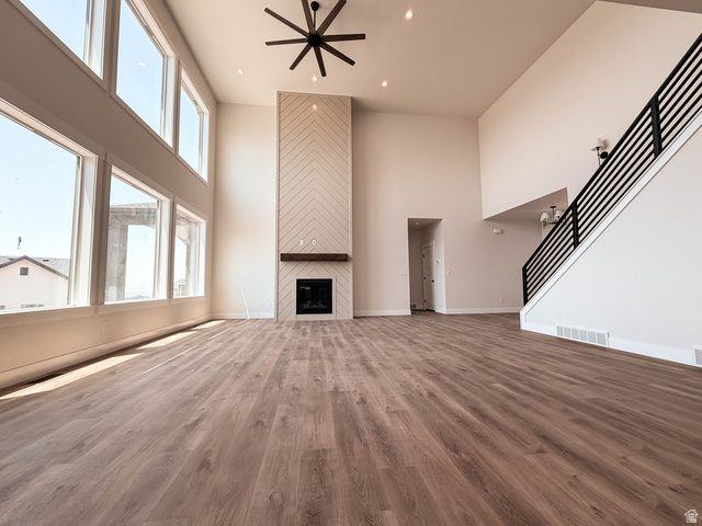 619 East Mountain Road North Ogden, UT 84414 - Photo 4 of 8 Spacious living area featuring double-height ceilings, a floor-to-ceiling fireplace with a chevron-patterned facade and wood mantel, large windows, wood-finish flooring, and a modern ceiling fan