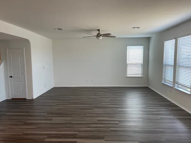 an empty room with wooden floor window and ceiling fan