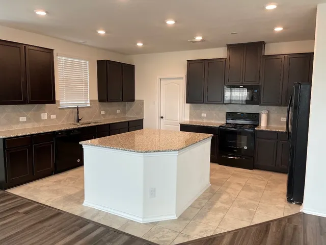 a kitchen with kitchen island granite countertop wooden cabinets a refrigerator and a sink