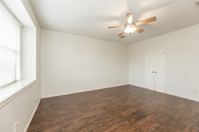 an empty room with wooden floor fan and windows