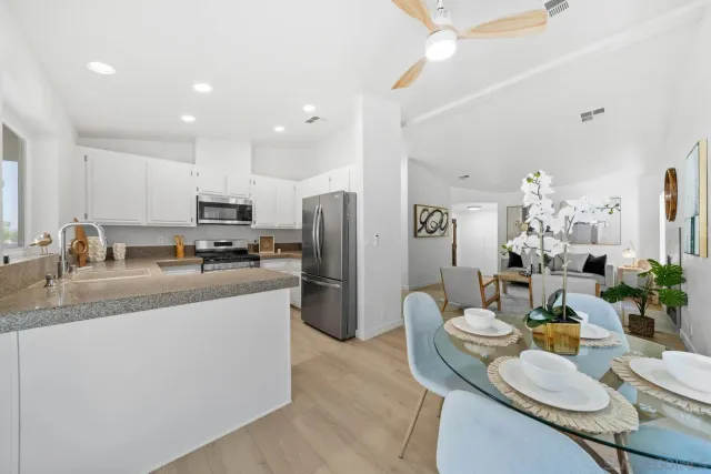 a kitchen with stainless steel appliances granite countertop a refrigerator a sink dishwasher a dining table and chairs with wooden floor