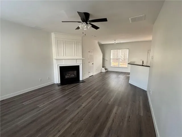 an empty room with wooden floor a ceiling fan a fireplace and windows