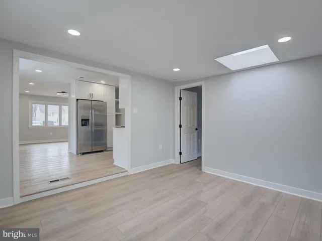 an empty room with wooden floor and entrance to kitchen