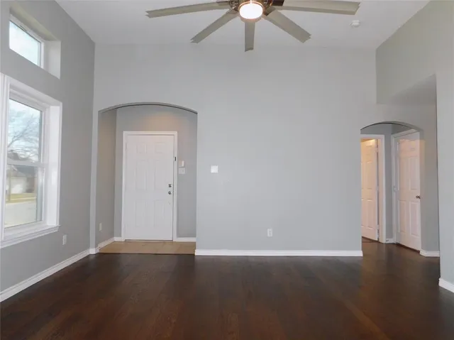 an empty room with wooden floor fan and windows