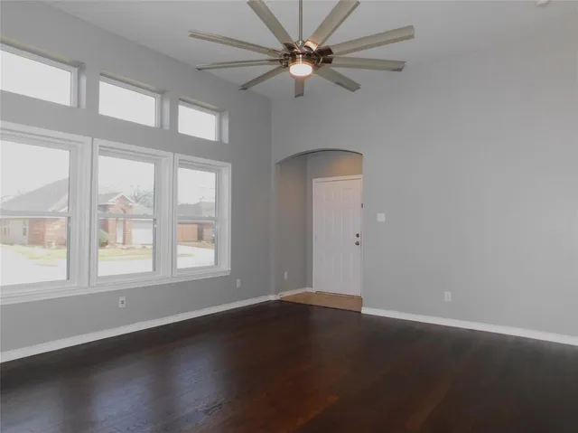 an empty room with wooden floor fan and windows