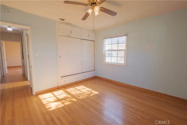 an empty room with wooden floor fan and windows