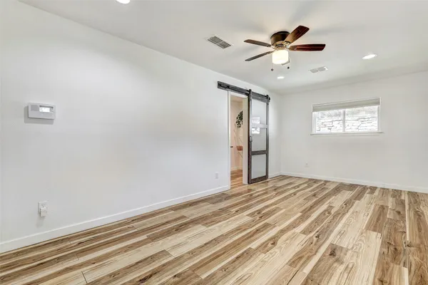 a view of an empty room with wooden floor and a ceiling fan