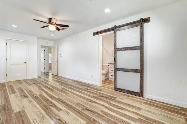 a view of an empty room with wooden floor and a ceiling fan