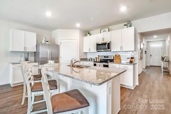 a kitchen with stainless steel appliances granite countertop a stove a sink a microwave a refrigerator and white cabinets with wooden floor