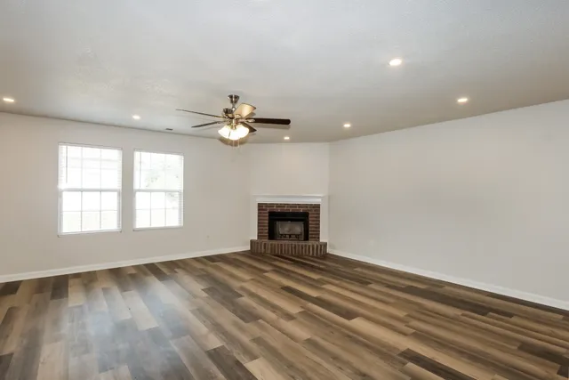 a view of an empty room with wooden floor fireplace and a window