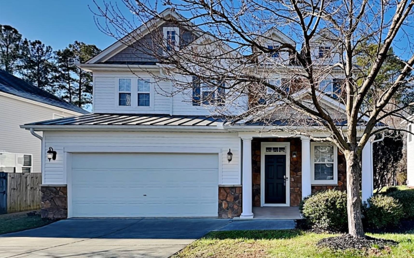 a view of a white house with large windows and a yard with plants and large tree