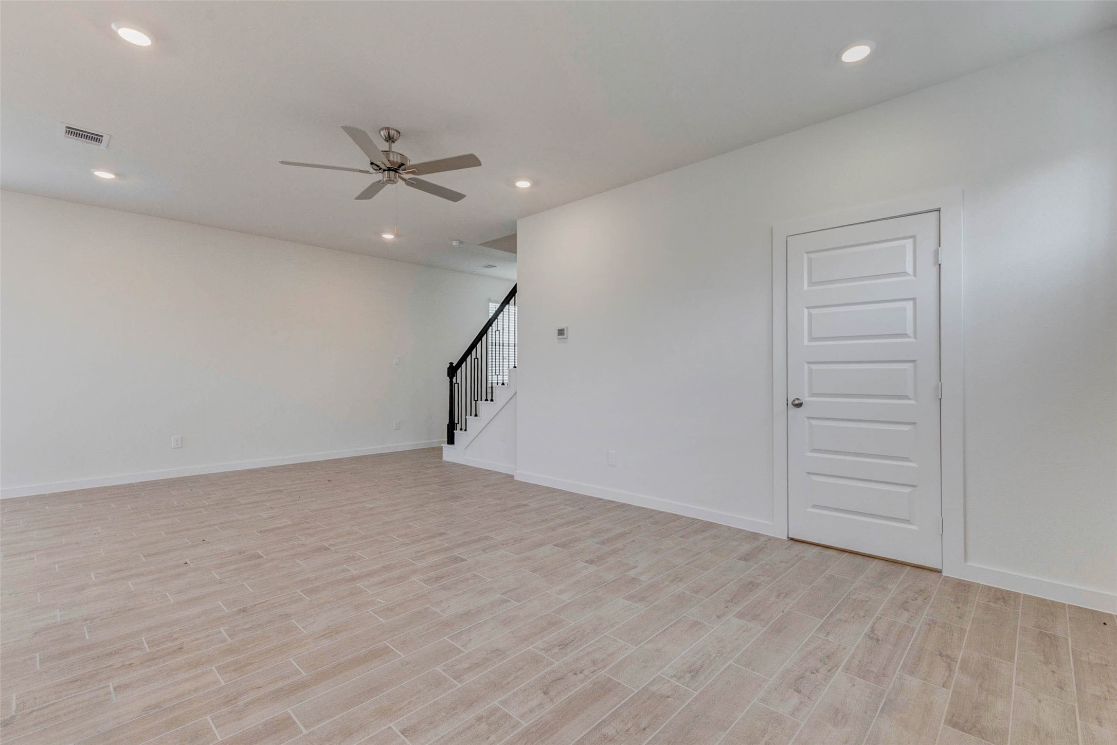 1131 Santee Court Rosharon, TX 77583 - Photo 14 of 31 Spacious and light-filled, this living area offers clean lines, neutral tones, and wood-look tile flooring. The ceiling fan adds comfort, while the adjacent stairway with wrought iron spindles provides an elegant visual anchor to the space.