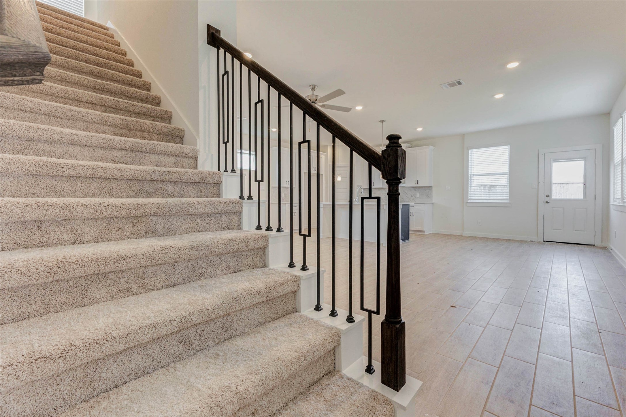 1131 Santee Court Rosharon, TX 77583 - Photo 17 of 31 The staircase serves as both a functional feature and focal point, with plush carpeting and a modern black wrought iron railing. Views of the open-plan main floor emphasize this home’s thoughtful flow and spacious design.