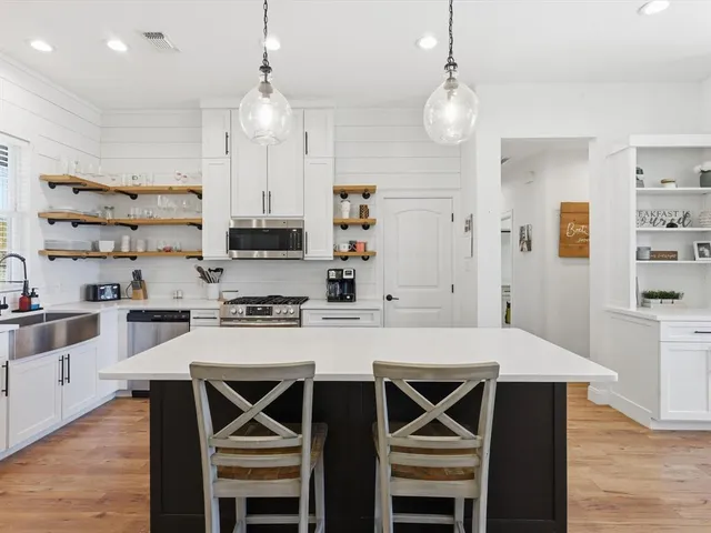 a kitchen with stainless steel appliances a stove a sink a kitchen island a stove a refrigerator a dining table and chairs with wooden floor