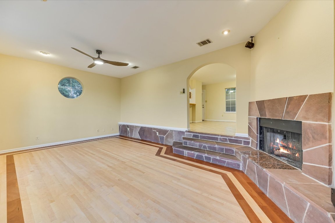 2405 Bahama Road Austin, TX 78733 - Photo 20 of 38 Unfurnished living room with wood finished floors, a tiled fireplace, a ceiling fan, and arched walkways