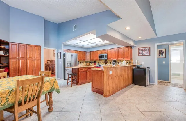 a kitchen with stainless steel appliances kitchen island granite countertop a refrigerator a sink a dining table and chairs