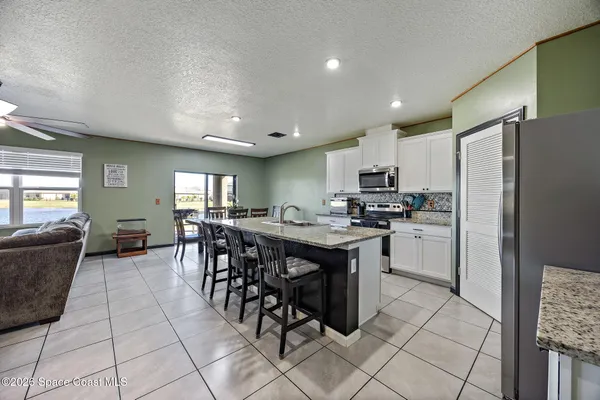 a kitchen with stainless steel appliances granite countertop a refrigerator a sink a stove a dining table and chairs with wooden floor