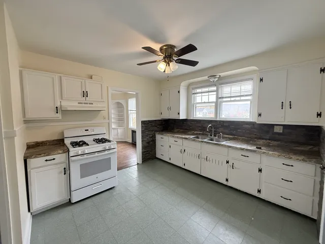 a kitchen with granite countertop a stove a sink and dishwasher with white cabinets