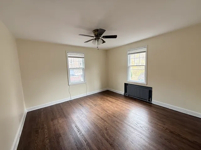 an empty room with wooden floor ceiling fan and windows