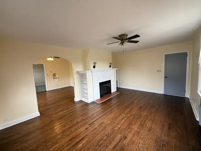 a view of a livingroom with a fireplace a ceiling fan and wooden floor