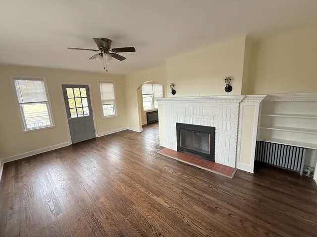 a view of an empty room with wooden floor fireplace and a window