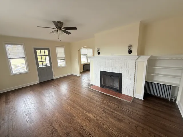 a view of an empty room with wooden floor fireplace and a window