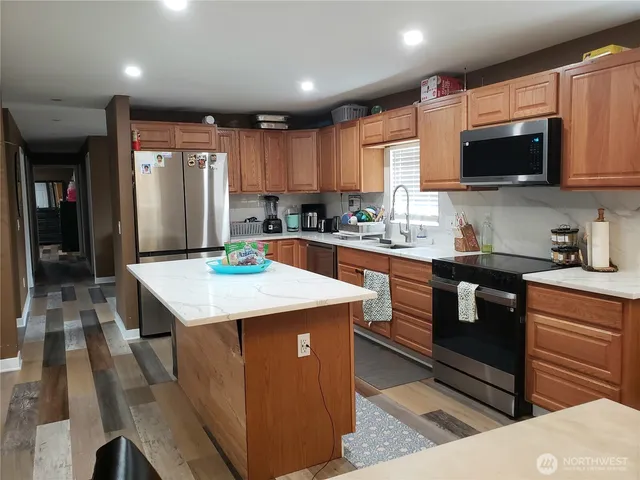 a kitchen with stainless steel appliances kitchen island granite countertop a sink a stove top oven a counter space and cabinets