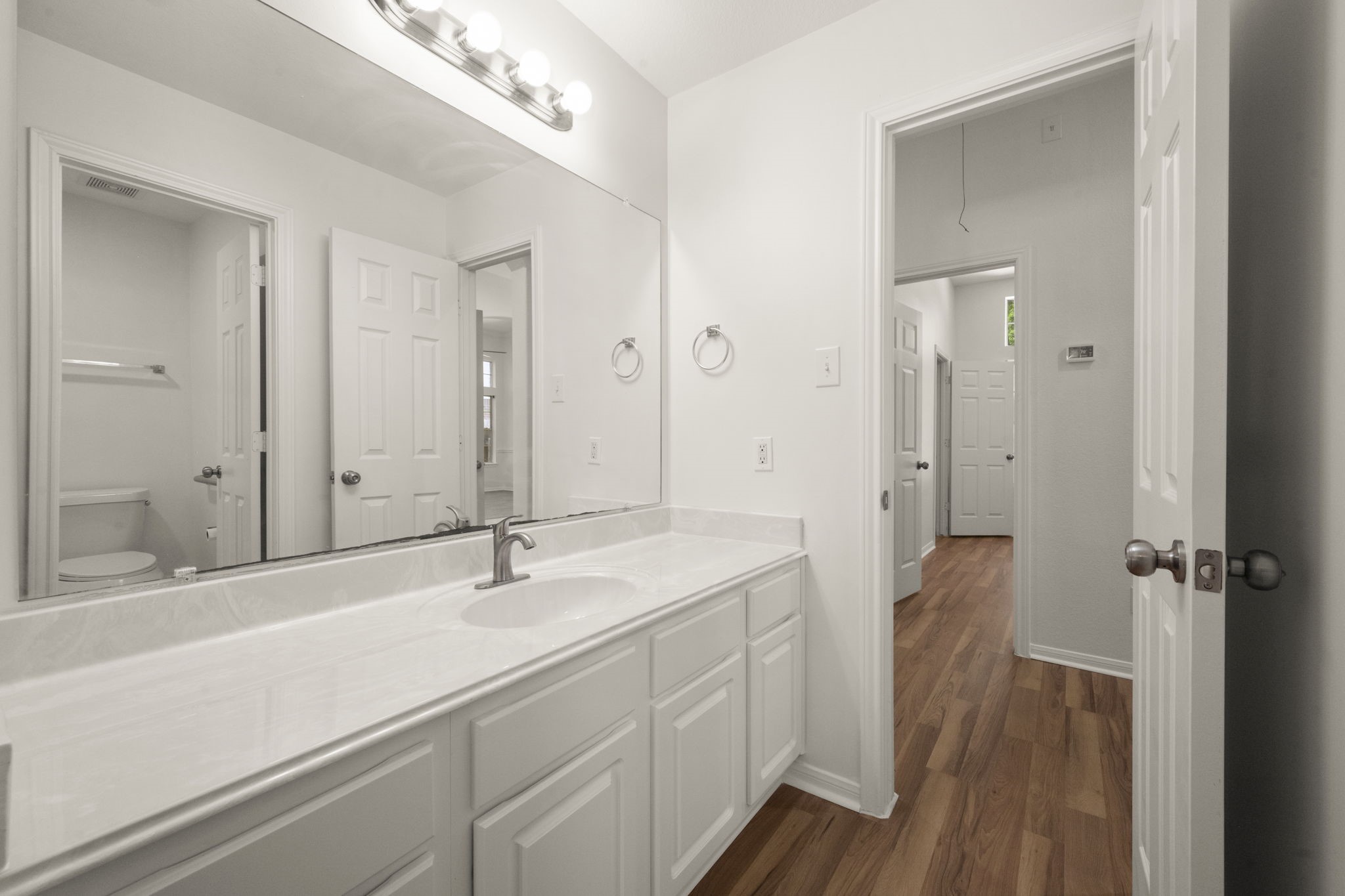 2018 Copperwood Park Lane Spring, TX 77386 - Photo 25 of 33 Bright and airy bathroom #2 with a large mirror, modern lighting, and a sleek white vanity. The space features wood flooring and offers convenient access to a hallway and adjacent room.