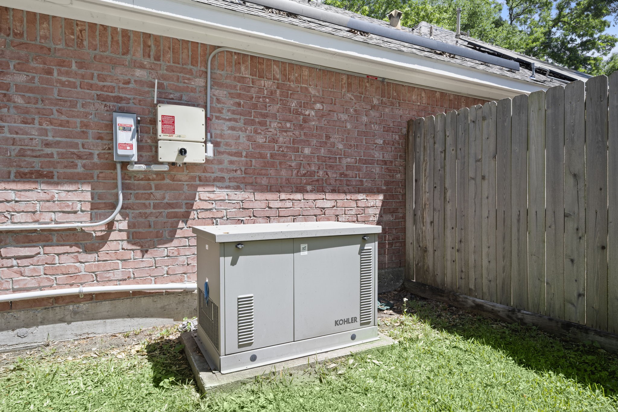 2018 Copperwood Park Lane Spring, TX 77386 - Photo 33 of 33 This photo shows an exterior view of a home with a brick wall, featuring a Kohler backup generator installed on a concrete pad. A wooden fence is adjacent, providing a private and secure setup.
