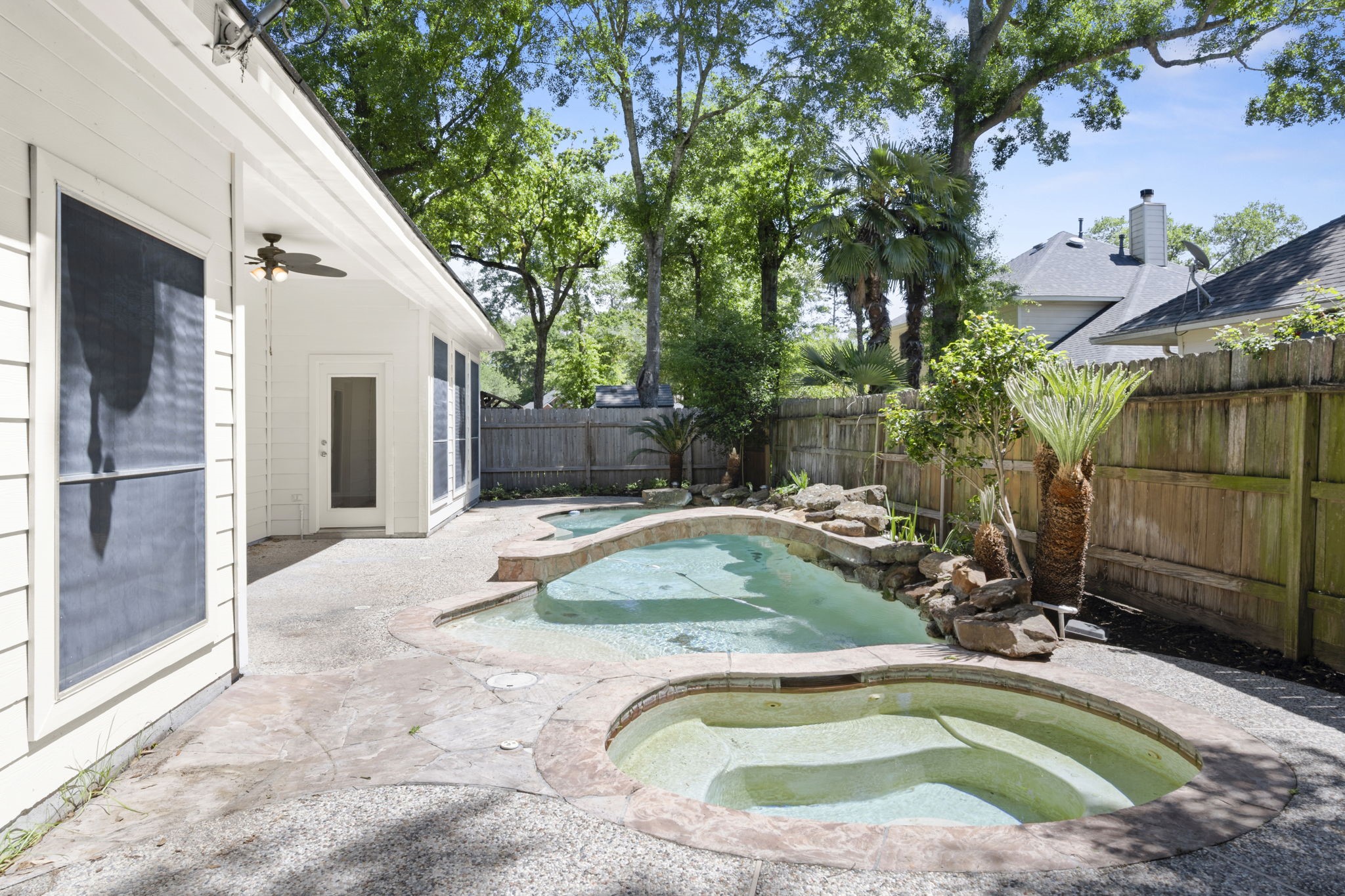 2018 Copperwood Park Lane Spring, TX 77386 - Photo 5 of 33 This backyard features a serene pool with a rock waterfall, surrounded by lush greenery and a privacy fence. The patio area includes a ceiling fan, offering a perfect spot for relaxation or entertaining.