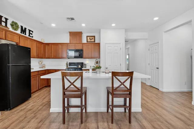 a kitchen with stainless steel appliances a refrigerator a stove top oven a sink dishwasher and a dining table with wooden floor