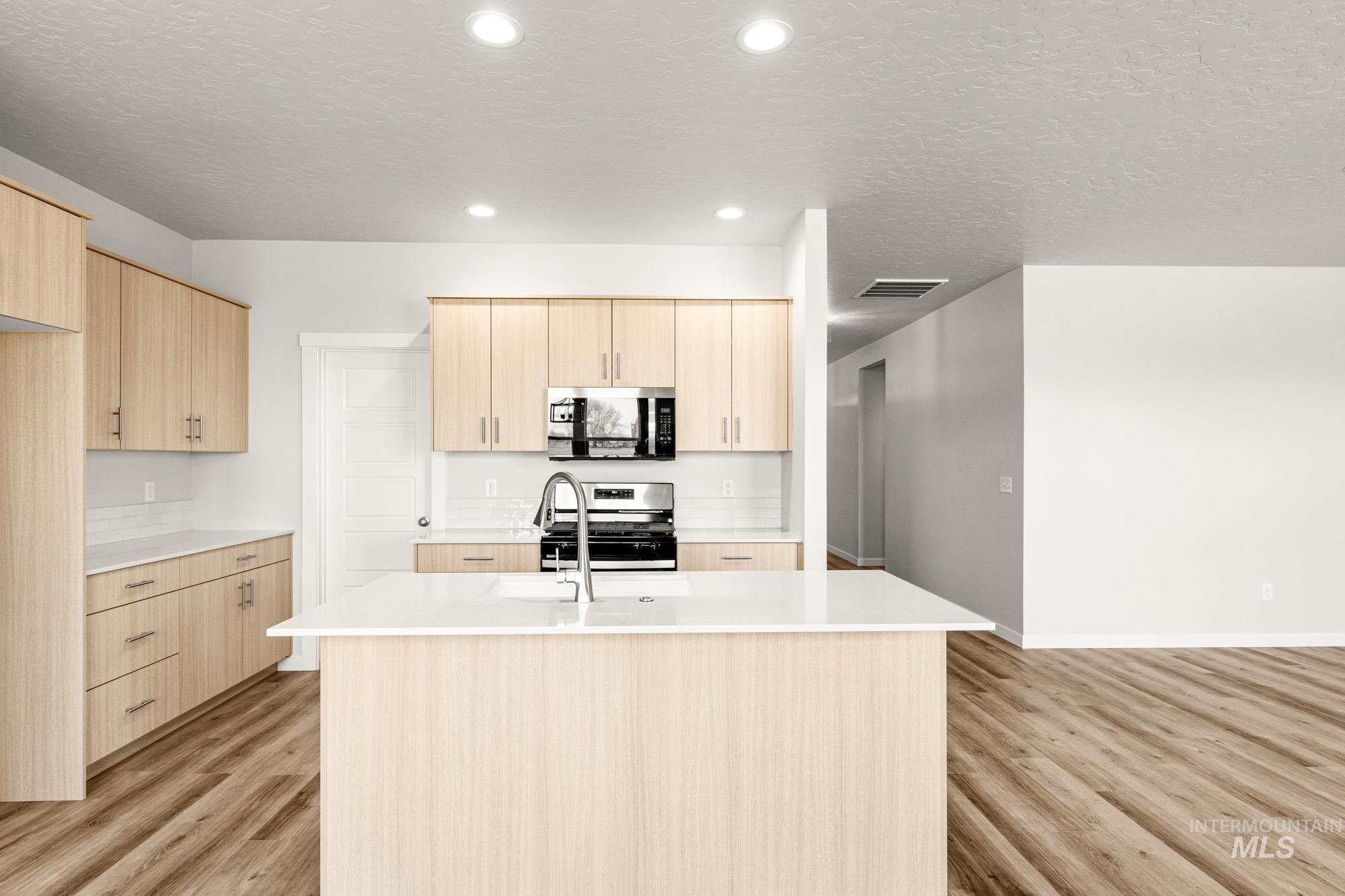 12865 Decatur Street Nampa, ID 83651 - Photo 3 of 20 Contemporary kitchen featuring a central island with an integrated sink, light wood-finish cabinetry, stainless steel appliances, white countertops, and wood-finish flooring
