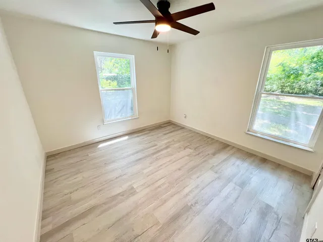 an empty room with wooden floor fan and windows