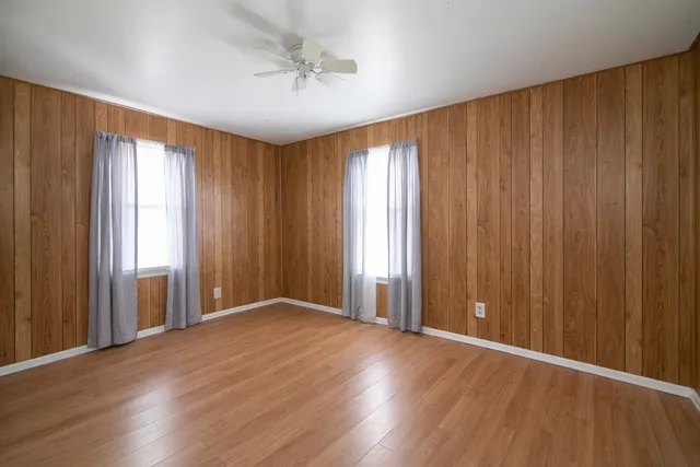an empty room with wooden floor and windows with curtains