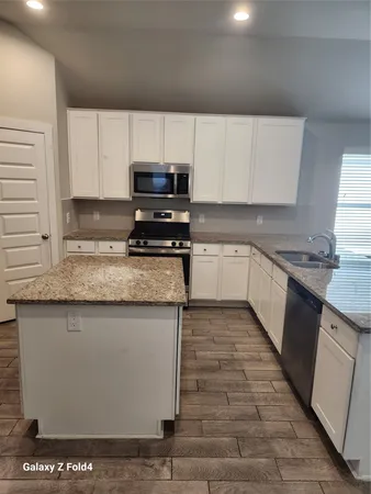 a kitchen with stainless steel appliances granite countertop a sink a stove top oven and white cabinets