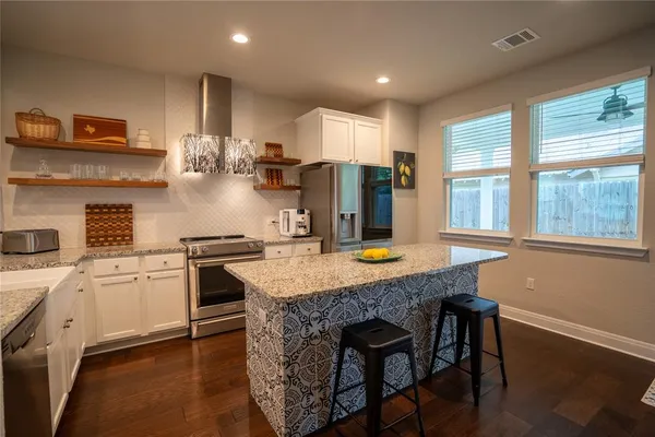 a kitchen with stainless steel appliances granite countertop a stove a sink a refrigerator and white cabinets with wooden floor