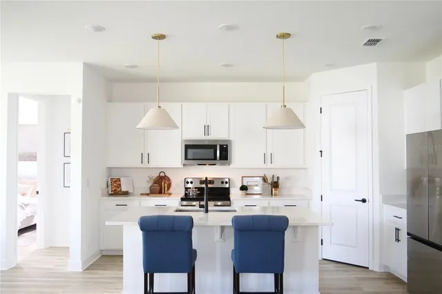 a kitchen with stainless steel appliances a refrigerator a stove a sink dishwasher and white cabinets with wooden floor