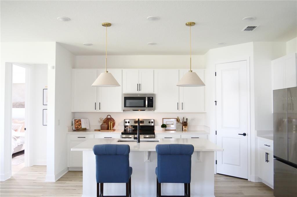 10337 Church Hammock Road Leesburg, FL 34788 - Photo 2 of 21 a kitchen with stainless steel appliances a refrigerator a stove a sink dishwasher and white cabinets with wooden floor