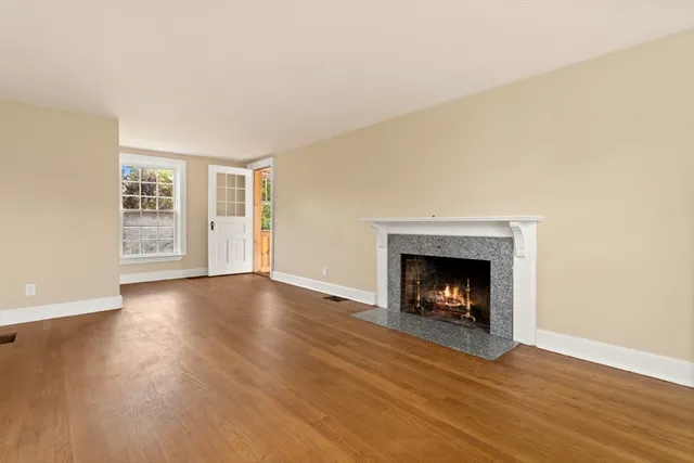 a view of an empty room with wooden floor fireplace and a window